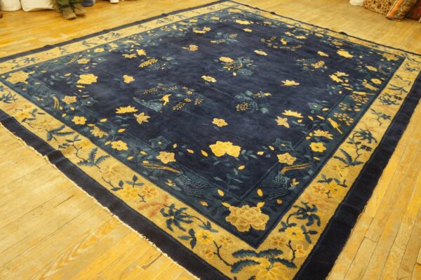 Square navy blue rug with gold and teal floral and bird patterns on light wood floors.