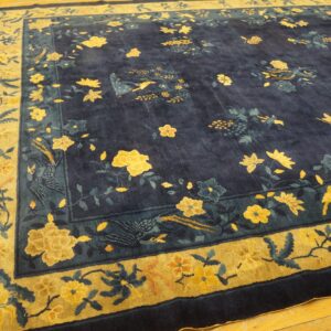 A deep indigo rug displays yellow and teal floral and bird motifs with a prominent gold and navy border on wood floors.