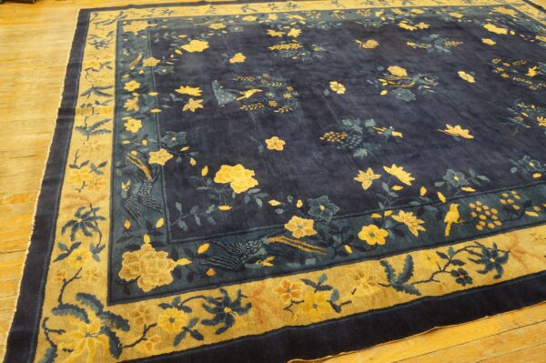 A deep indigo rug displays yellow and teal floral and bird motifs with a prominent gold and navy border on wood floors.