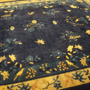 Dark navy rug featuring scattered gold and blue floral and bird motifs, lying on wood flooring.