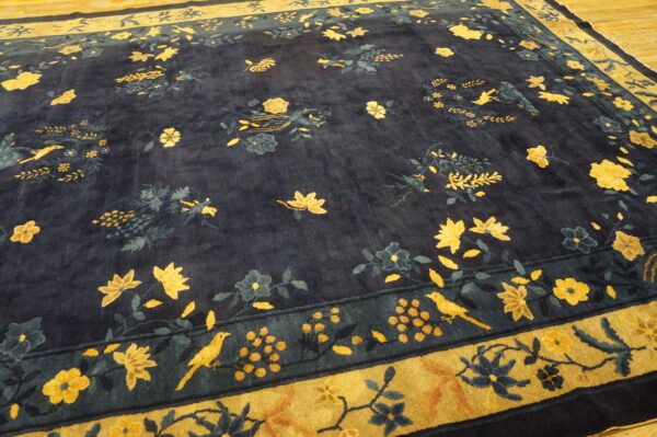Dark navy rug featuring scattered gold and blue floral and bird motifs, lying on wood flooring.