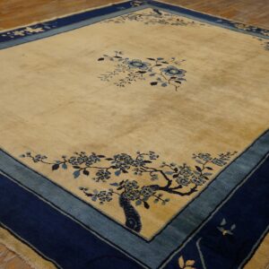 Gold square rug featuring navy and light blue botanical motifs and thick borders on wood planks.