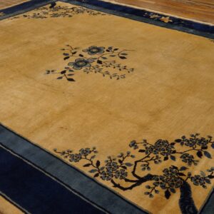 A golden rug with navy and teal borders features delicate blue floral patterns on distressed wooden flooring.