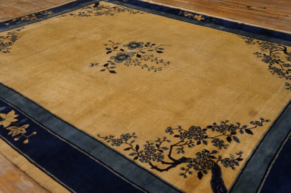 A golden rug with navy and teal borders features delicate blue floral patterns on distressed wooden flooring.
