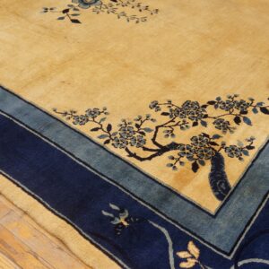 A golden yellow rug with blue floral branches and a layered blue border sits on wood planks.