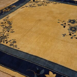 High-pile gold rug featuring a navy blue and dusty blue floral border over light wood plank flooring.