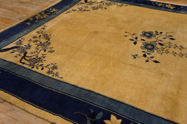 High-pile gold rug featuring a navy blue and dusty blue floral border over light wood plank flooring.