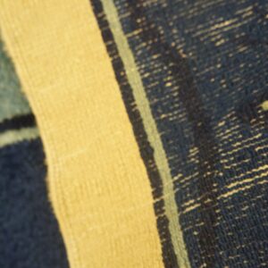 Detailed view of a striped rug featuring yellow, coarse dark blue, and thin light blue color bands.