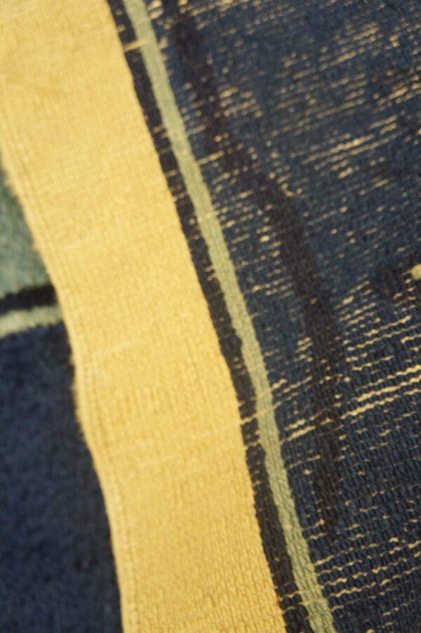 Detailed view of a striped rug featuring yellow, coarse dark blue, and thin light blue color bands.