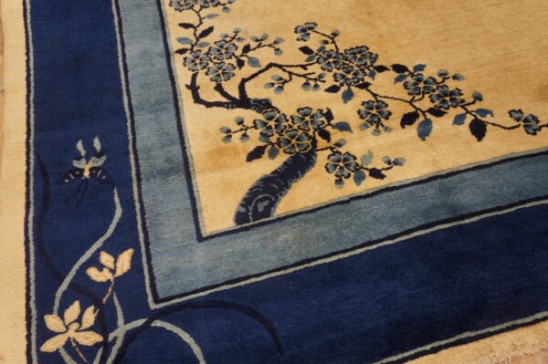 Navy and dusty blue floral vine pattern on a tan field, framed by a multi-banded border.