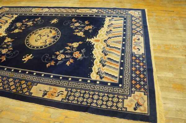 Navy blue rug displays gold floral sprays, a bird medallion, and complex borders on light wooden flooring.
