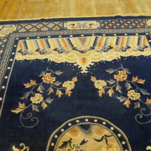 Deep blue rug with large floral vines and complex borders sits on distressed wood flooring.