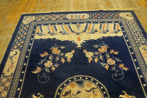 Deep blue rug with large floral vines and complex borders sits on distressed wood flooring.