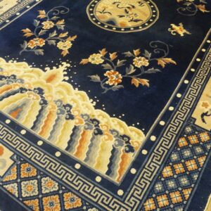 Plush navy blue rug with stylized floral, wave, and geometric patterns rests on light wood flooring.