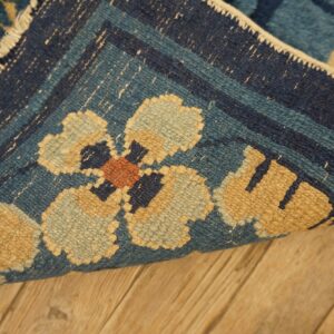 Detail view of a navy and teal rug with geometric floral designs lying on light brown wood flooring.
