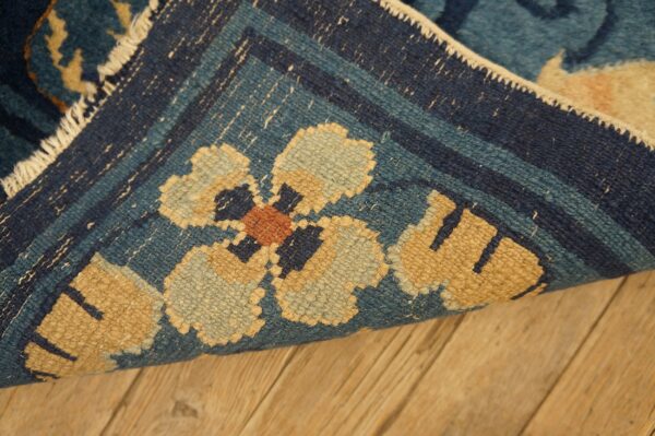 Detail view of a navy and teal rug with geometric floral designs lying on light brown wood flooring.