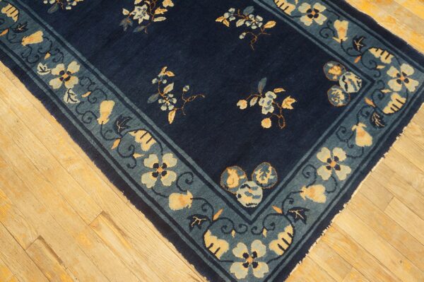 Navy blue rug with scattered yellow and pale blue floral motifs and a teal border on light wood flooring.
