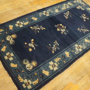 Navy blue rug with a teal and yellow floral border on a rustic light wood floor.