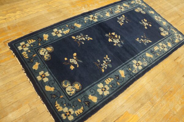 Navy blue rug with a teal and yellow floral border on a rustic light wood floor.
