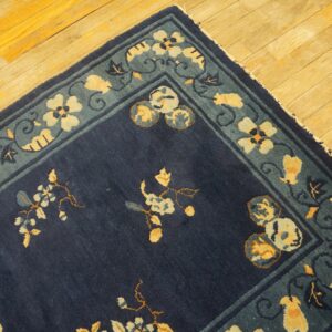 A corner of a dark blue rug with intricate yellow and blue floral motifs rests on golden hardwood floors.