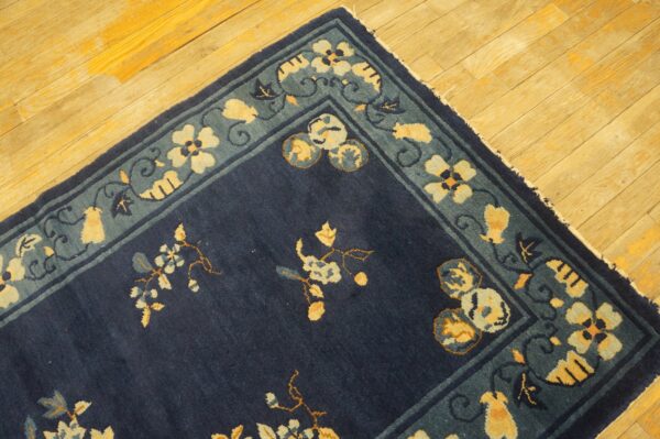 A corner of a dark blue rug with intricate yellow and blue floral motifs rests on golden hardwood floors.
