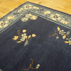 Navy blue rug with cream and light blue floral patterns and a wide border rests on wood flooring.