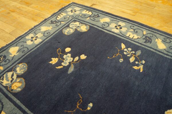 Navy blue rug with cream and light blue floral patterns and a wide border rests on wood flooring.