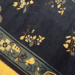 Deep blue rug with yellow and slate floral motifs and a patterned blue border on hardwood flooring.