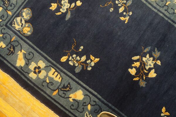 Deep blue rug with yellow and slate floral motifs and a patterned blue border on hardwood flooring.
