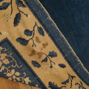 Dark blue rug with a tan botanical border pattern resting on light brown wood flooring.
