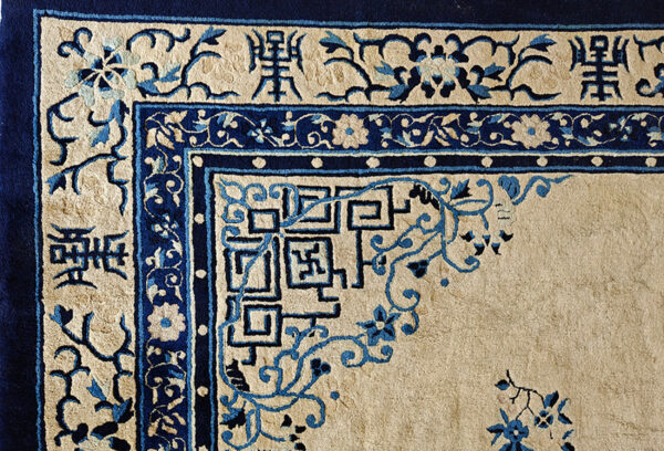 The corner of a high-pile beige rug with dark blue borders and traditional symbolic characters.