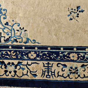 Corner detail of a rug showing beige field, navy blue scrolling vines, geometric key patterns, and multi-banded floral borders.