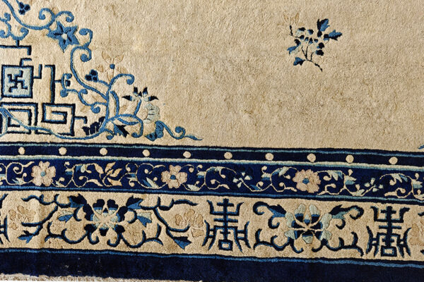 Corner detail of a rug showing beige field, navy blue scrolling vines, geometric key patterns, and multi-banded floral borders.