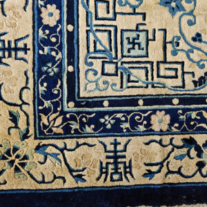 Intricate blue and tan rug border detail showing geometric fretwork, stylized floral designs, and symbols.