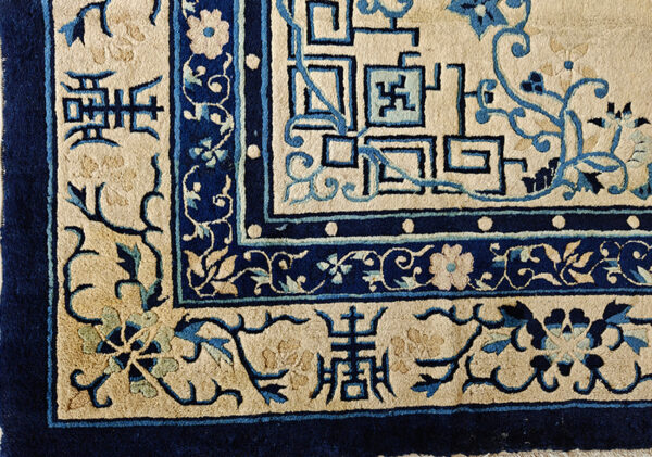 Intricate blue and tan rug border detail showing geometric fretwork, stylized floral designs, and symbols.