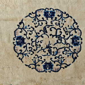 Close-up detail of a beige rug featuring a circular blue, navy, and pink scrolling floral medallion.