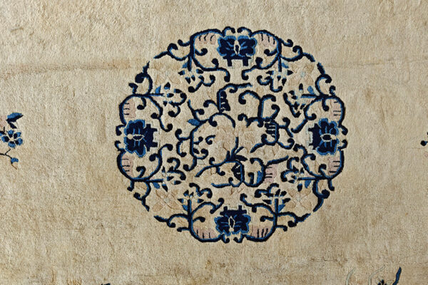 Close-up detail of a beige rug featuring a circular blue, navy, and pink scrolling floral medallion.