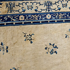 Detail of a low-pile beige rug with complex navy blue borders and sparse blue floral motifs.