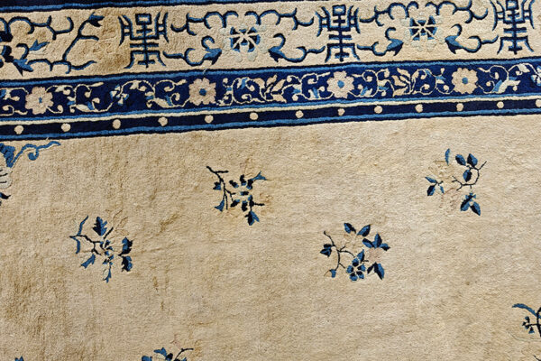 Detail of a low-pile beige rug with complex navy blue borders and sparse blue floral motifs.