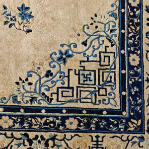 Detail shot of a rug corner with beige field and complex blue traditional floral and angular border motifs.