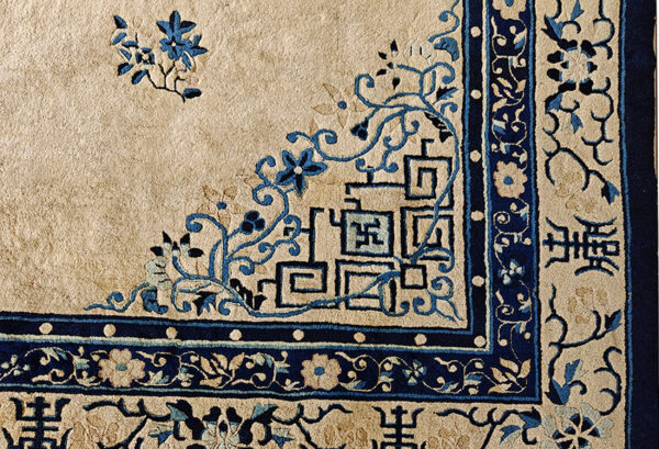 Detail shot of a rug corner with beige field and complex blue traditional floral and angular border motifs.