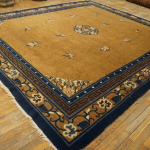 A large golden-brown rug with a wide navy blue and tan detailed border sits on worn wood floors.