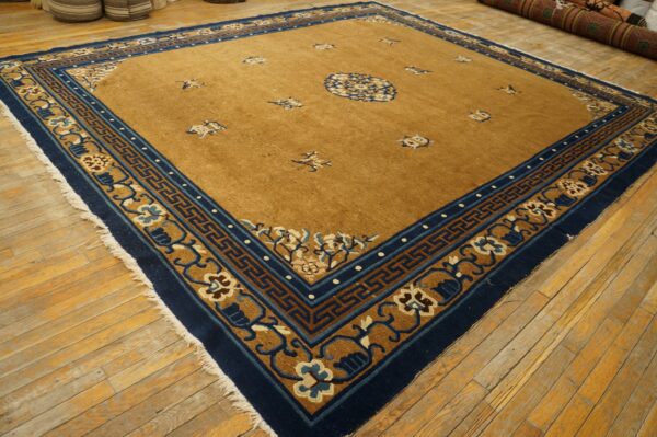 A large golden-brown rug with a wide navy blue and tan detailed border sits on worn wood floors.