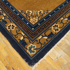 A brown and navy rug corner with floral and key patterns rests on distressed golden wood flooring.
