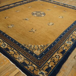 Gold rug with scattered navy motifs and a wide geometric and floral blue border on wood floors.
