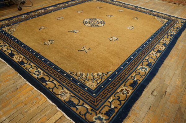 Gold rug with scattered navy motifs and a wide geometric and floral blue border on wood floors.