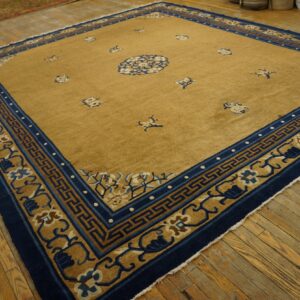 Tan rug featuring a central blue medallion and navy, patterned borders on distressed wood flooring.