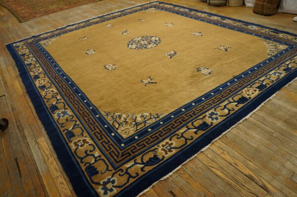 Tan rug featuring a central blue medallion and navy, patterned borders on distressed wood flooring.