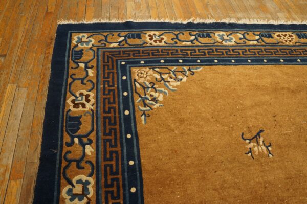 Golden brown rug corner with navy and tan scrolling borders and fringe visible on wood flooring.