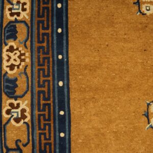 Golden yellow rug border featuring navy Greek key and floral designs lies on bright hardwood flooring.